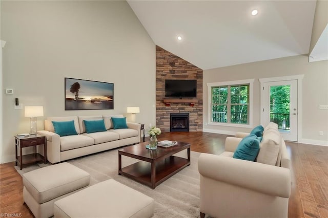 living room with hardwood / wood-style flooring, high vaulted ceiling, and a stone fireplace