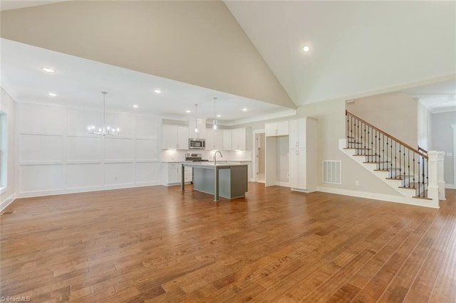 unfurnished living room with light wood-type flooring, crown molding, high vaulted ceiling, and a chandelier