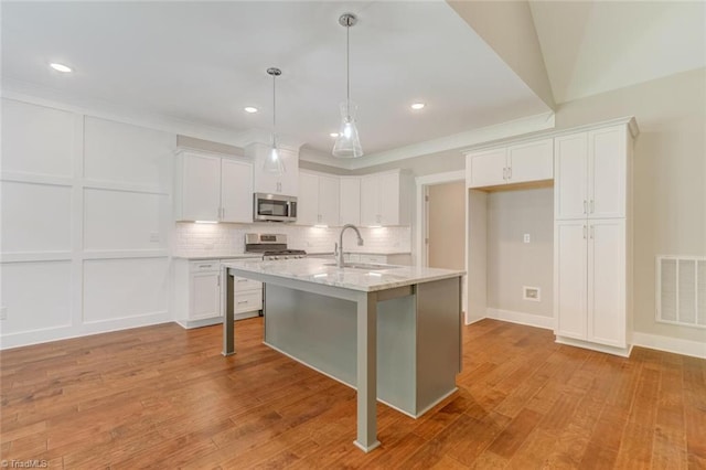 kitchen featuring light wood-type flooring, appliances with stainless steel finishes, a kitchen island with sink, and white cabinets