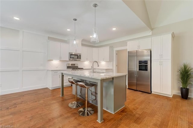 kitchen with stainless steel appliances, light hardwood / wood-style floors, white cabinetry, a kitchen breakfast bar, and a center island with sink