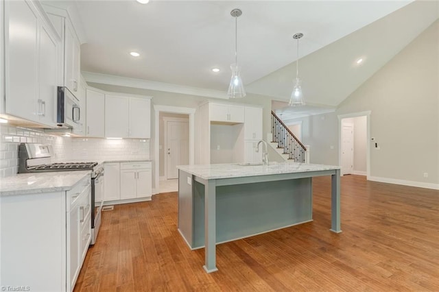 kitchen featuring light stone countertops, appliances with stainless steel finishes, a center island with sink, white cabinets, and light hardwood / wood-style floors