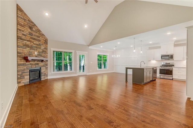 unfurnished living room featuring a fireplace, sink, high vaulted ceiling, and light hardwood / wood-style floors