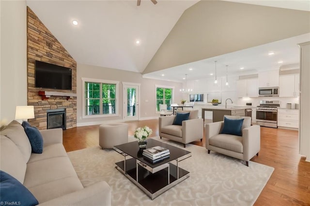 living room featuring light wood-type flooring, high vaulted ceiling, sink, and a stone fireplace