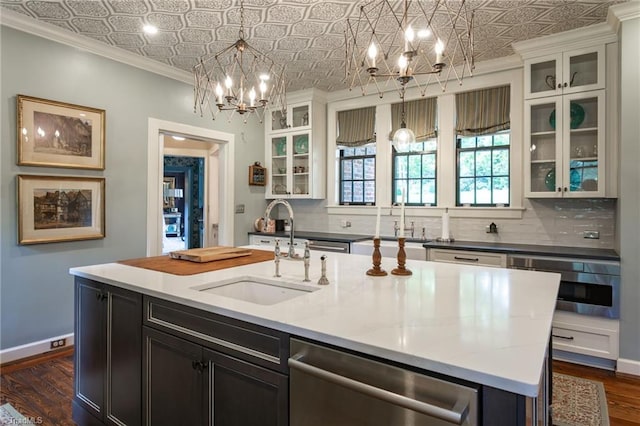 kitchen with a notable chandelier, decorative light fixtures, sink, an island with sink, and decorative backsplash