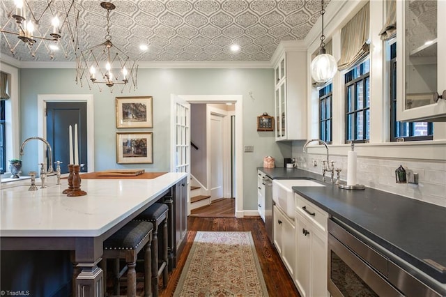 kitchen with crown molding, white cabinetry, sink, and hanging light fixtures