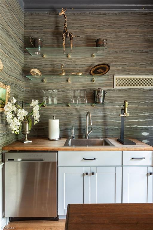 bar featuring butcher block countertops, dishwasher, light hardwood / wood-style flooring, sink, and white cabinets