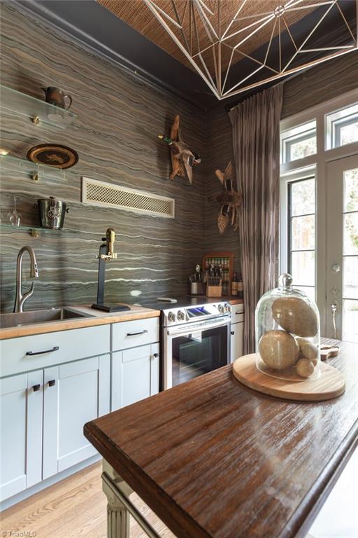 kitchen featuring stainless steel electric range, white cabinets, light wood-type flooring, sink, and butcher block counters