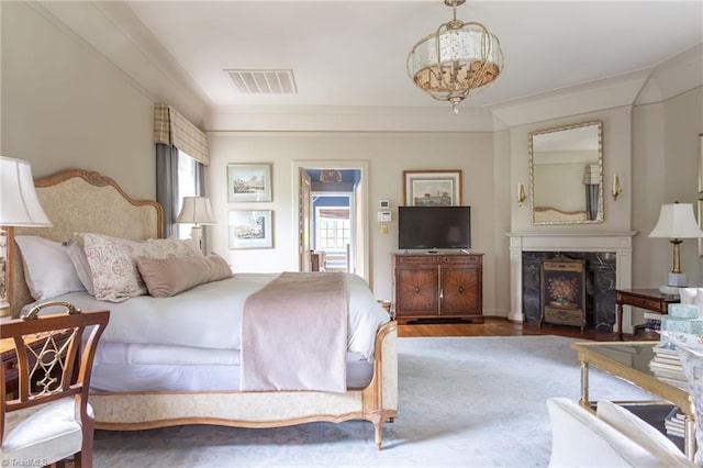 bedroom featuring a fireplace, crown molding, a chandelier, and hardwood / wood-style floors