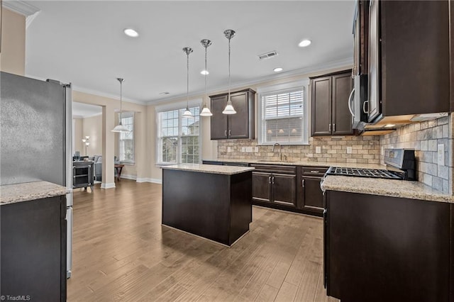 kitchen featuring appliances with stainless steel finishes, a center island, decorative light fixtures, and light hardwood / wood-style flooring