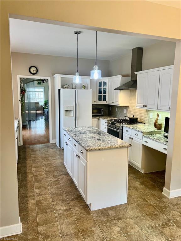 kitchen featuring stainless steel gas range oven, backsplash, wall chimney exhaust hood, and white cabinets