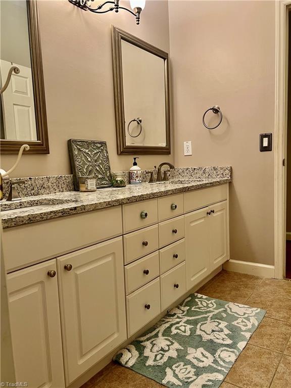 bathroom with double vanity, baseboards, tile patterned floors, and a sink