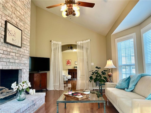 living area featuring a brick fireplace, wood finished floors, a ceiling fan, and vaulted ceiling