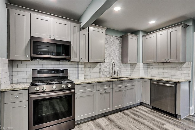 kitchen with appliances with stainless steel finishes, light wood-type flooring, gray cabinets, and a sink