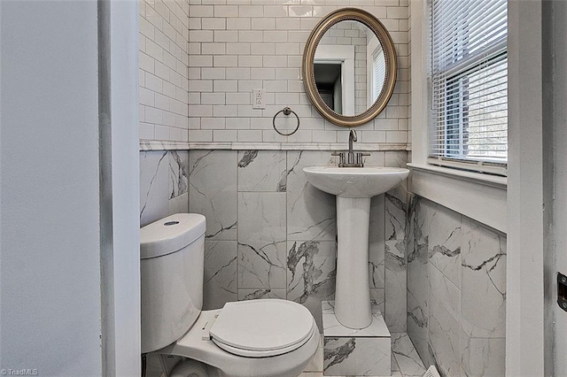 bathroom with toilet, marble finish floor, and tile walls