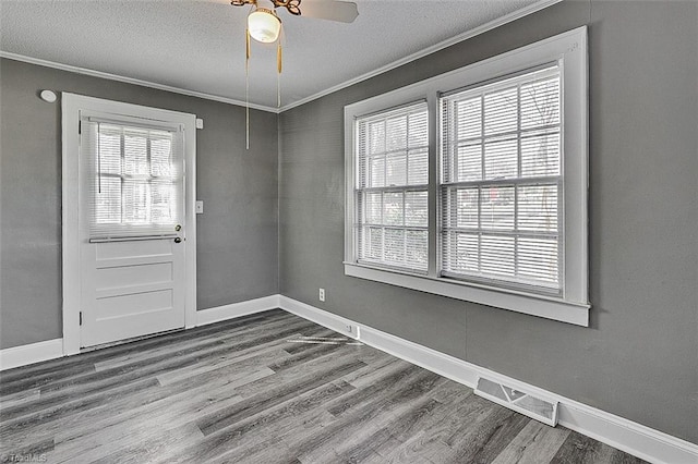 interior space with dark wood-style floors, a healthy amount of sunlight, visible vents, and crown molding