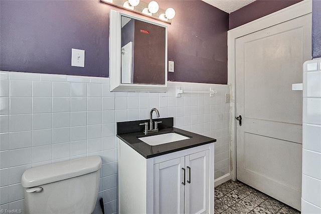 half bath featuring toilet, a wainscoted wall, tile walls, and vanity