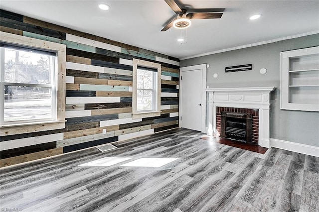 living room with recessed lighting, ornamental molding, a brick fireplace, wood walls, and wood finished floors