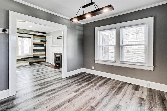 unfurnished dining area featuring ornamental molding, a fireplace, baseboards, and wood finished floors