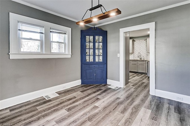 entryway with baseboards, visible vents, wood finished floors, and ornamental molding