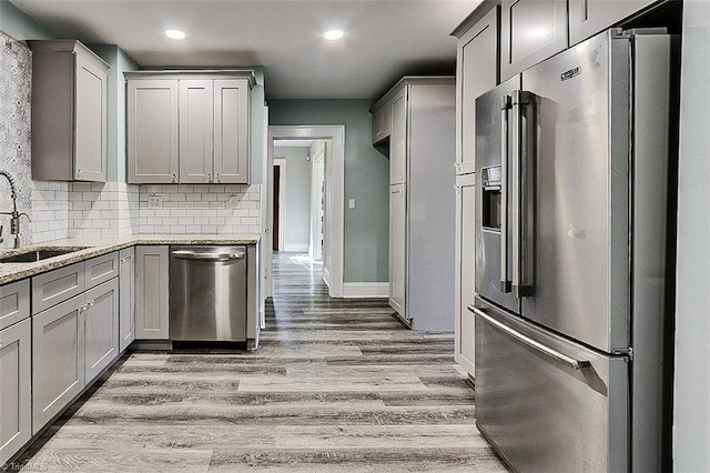 kitchen featuring light stone counters, light wood-style flooring, gray cabinetry, appliances with stainless steel finishes, and a sink