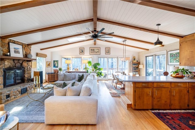 living room featuring light hardwood / wood-style floors, vaulted ceiling with skylight, wood ceiling, ceiling fan, and a stone fireplace