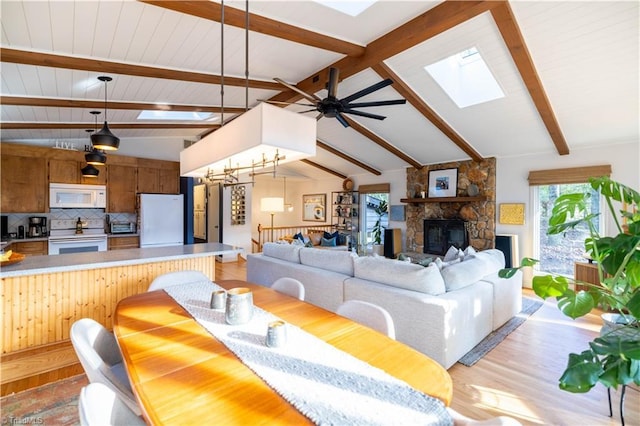 living room featuring ceiling fan with notable chandelier, a fireplace, light hardwood / wood-style floors, and lofted ceiling with skylight