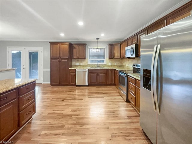 kitchen featuring appliances with stainless steel finishes, sink, pendant lighting, light hardwood / wood-style floors, and light stone countertops