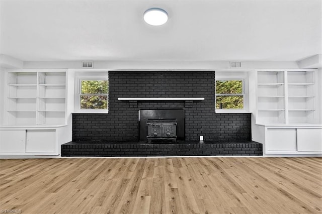 unfurnished living room featuring a wood stove, plenty of natural light, built in features, and light wood-type flooring