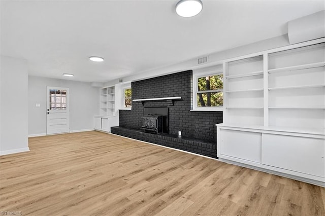 unfurnished living room featuring built in shelves, plenty of natural light, and light hardwood / wood-style floors