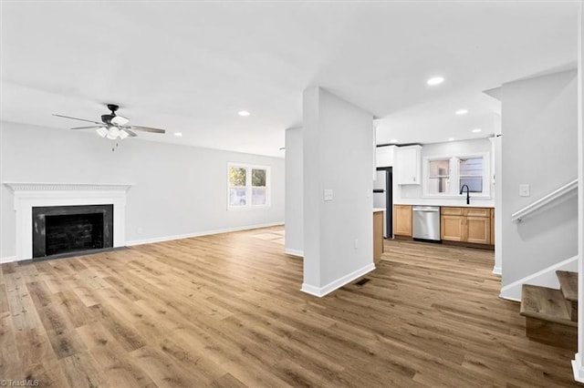 unfurnished living room with ceiling fan, sink, and light wood-type flooring