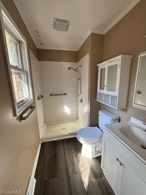 bathroom featuring tiled shower, vanity, wood-type flooring, a textured ceiling, and toilet