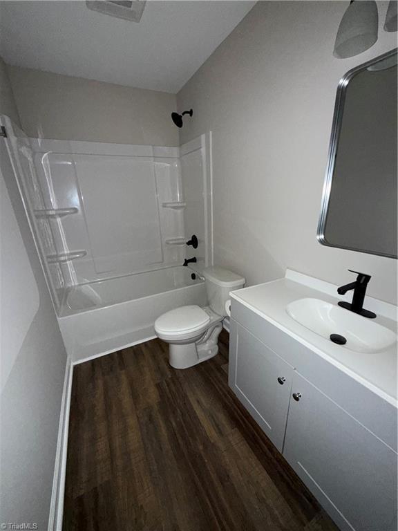 full bathroom with hardwood / wood-style flooring, washtub / shower combination, toilet, and vanity