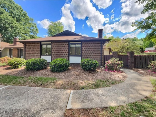 view of side of home featuring a chimney, brick siding, and fence
