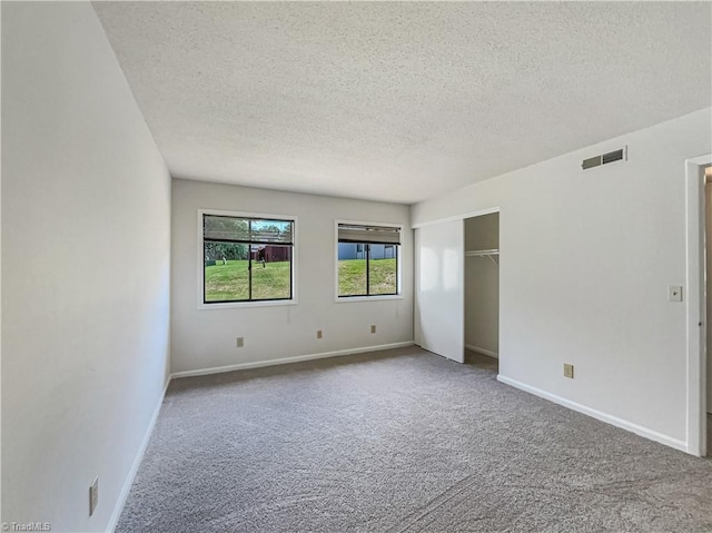 unfurnished room with a textured ceiling, carpet flooring, and baseboards