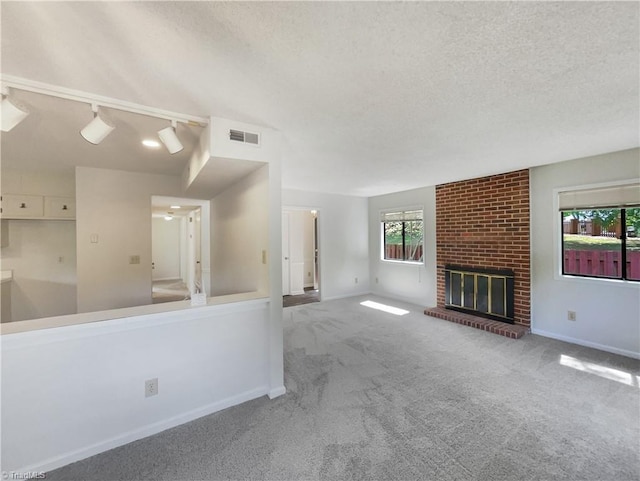 unfurnished living room featuring a textured ceiling, carpet, baseboards, a brick fireplace, and track lighting