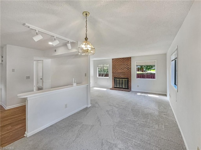 unfurnished living room with a textured ceiling, a chandelier, rail lighting, and baseboards