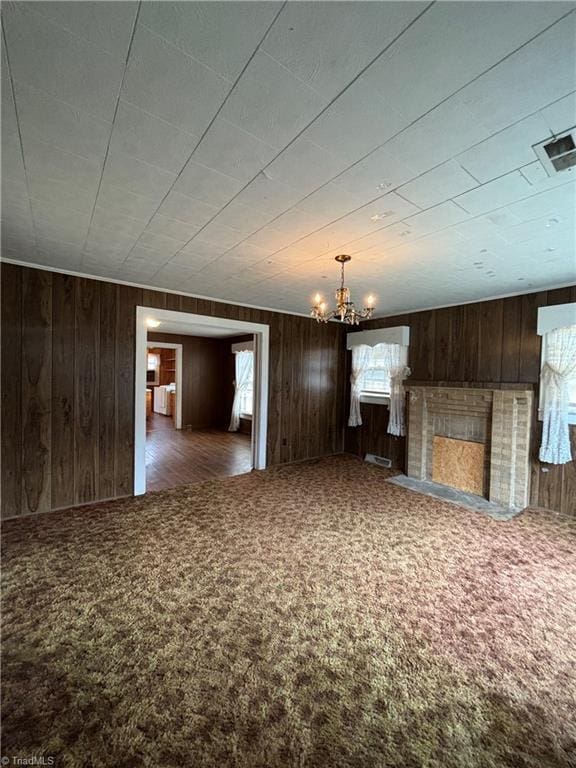 unfurnished living room with a notable chandelier, dark carpet, and wooden walls