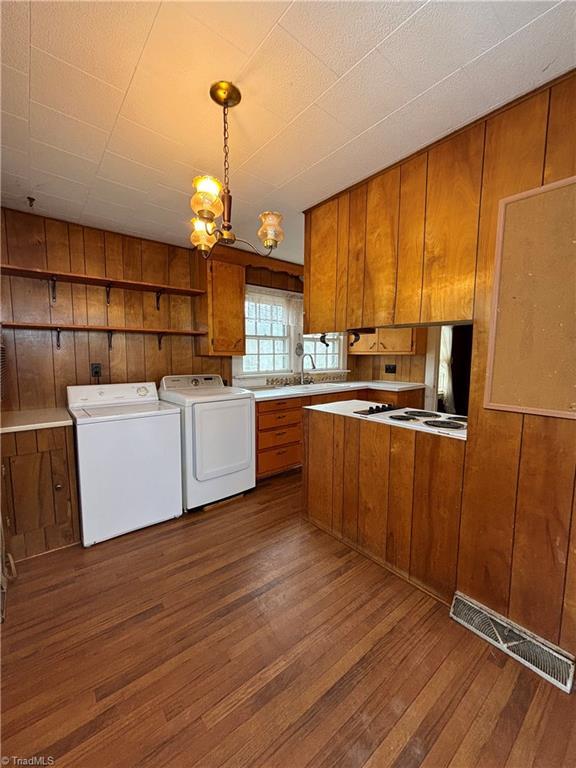 kitchen featuring dark wood-type flooring, hanging light fixtures, white gas stovetop, wooden walls, and washer and clothes dryer