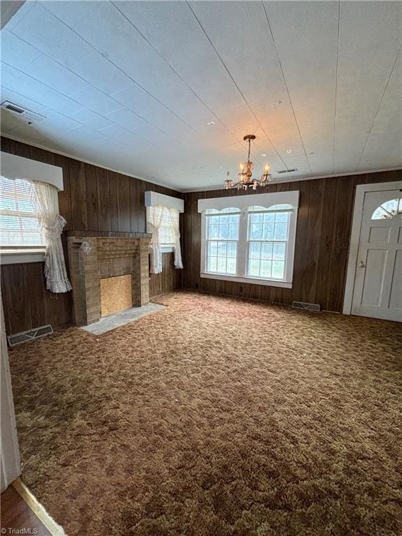 unfurnished living room featuring carpet flooring, wooden walls, and a chandelier