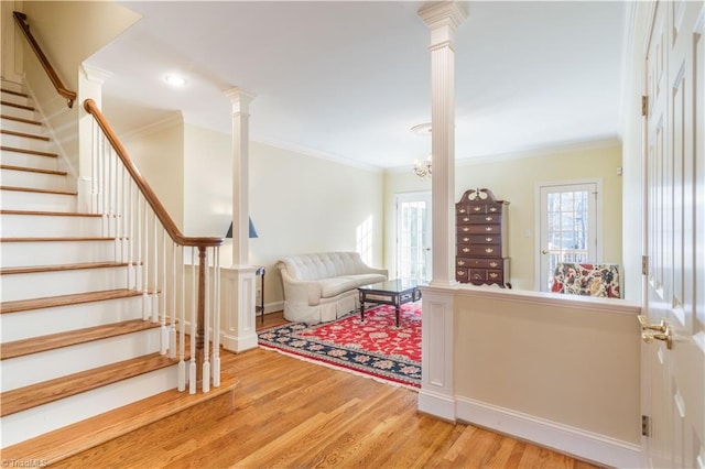 living room featuring decorative columns, ornamental molding, a notable chandelier, and hardwood / wood-style flooring