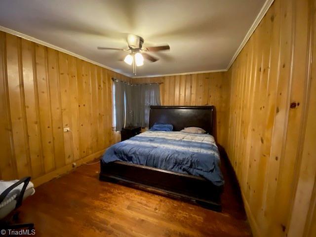 bedroom featuring crown molding, ceiling fan, wood-type flooring, and wood walls