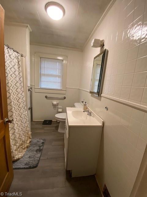 bathroom featuring hardwood / wood-style floors, tile walls, vanity, toilet, and crown molding