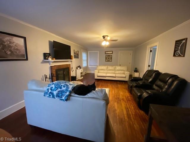 living room with dark wood-type flooring, ornamental molding, and a brick fireplace