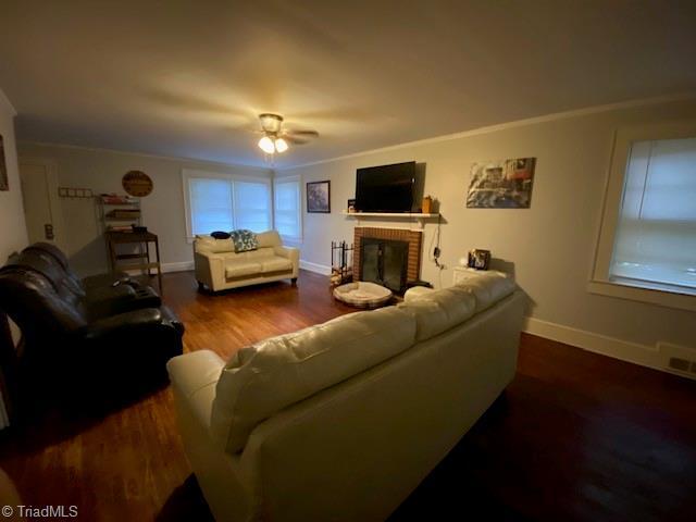 living room featuring crown molding, dark hardwood / wood-style floors, ceiling fan, and a fireplace