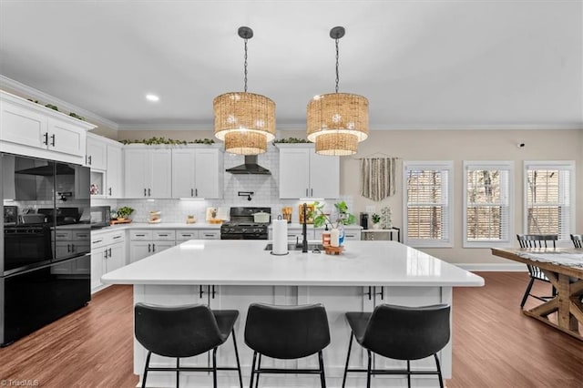 kitchen with wood finished floors, black appliances, light countertops, crown molding, and a kitchen breakfast bar