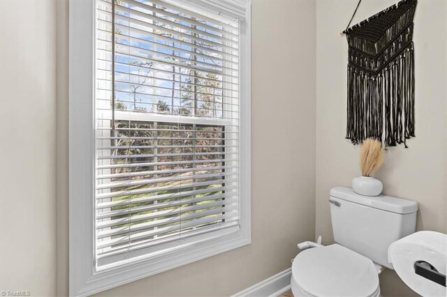 half bath featuring toilet, baseboards, and a wealth of natural light