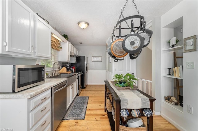 kitchen featuring white cabinetry, a textured ceiling, a sink, light wood finished floors, and stainless steel appliances