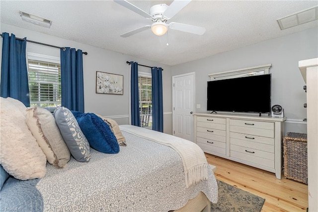 bedroom with a ceiling fan, a textured ceiling, visible vents, and light wood-style flooring