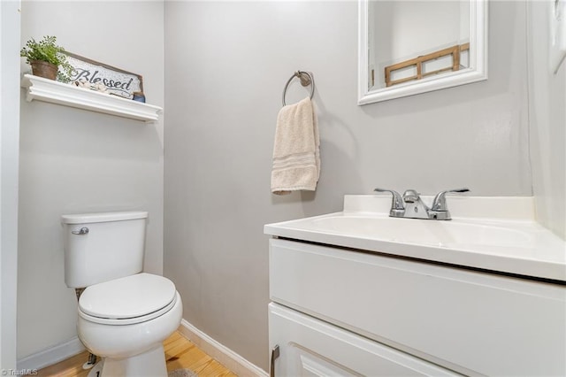 bathroom featuring toilet, baseboards, wood finished floors, and vanity