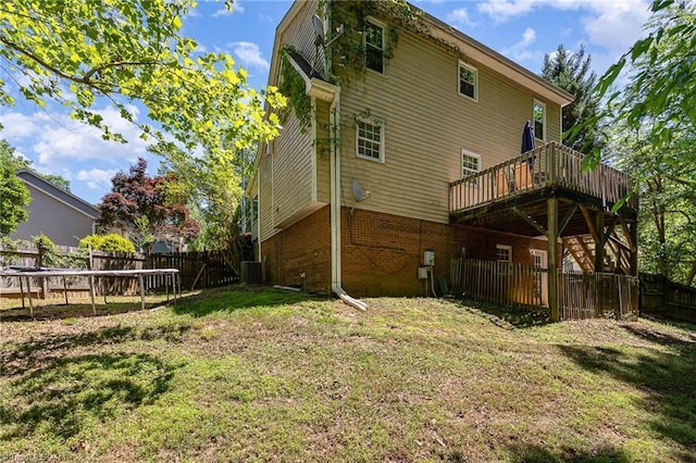 back of property with a wooden deck, cooling unit, a fenced backyard, brick siding, and a yard